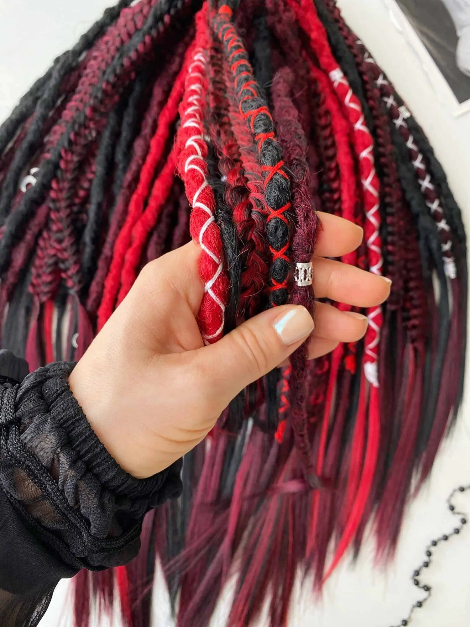 Hand close-up of Bloodmoon textured dread extensions — black, red and marled strands