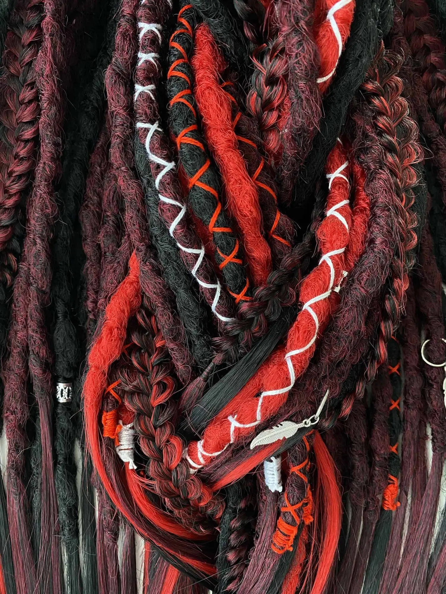 Bloodmoon textured dreads macro — white and red X-pattern thread wraps with silver feather charm